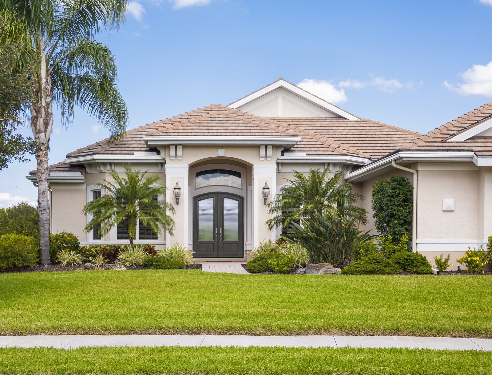 New upscale contemporary home with palm trees, front lawn and sidewalk. Tropical climate.